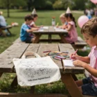 Kids color at picnic tables with Crafty Folding Calico Bags and crayons outdoors.