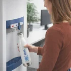 Woman refilling a Vitasip Double Wall Drink Bottle at an office water dispenser.