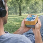 A person with headphones holds a Gig Bamboo Bluetooth Speakers outdoors.