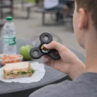 Person holding a Full Colour Printed Spinner near a table with a sandwich, apple, and water bottle.