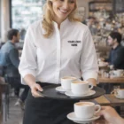 Smiling server in a Ladies 3/4 Sleeve Continental Shirt serves coffee in a bustling café.