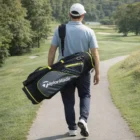 Man carrying a Taylormade Select Lx Black Lime Cart Bag on a golf course path.