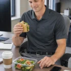Smiling man at desk in Nike Dri-Fit Micro Pique 2.0 Pocket Polo with salad, coffee & phone.