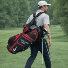 Man carrying a red Nike Sport 2 Stand Bag with clubs, logo displayed, on golf course.