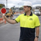 Construction worker in a Breathable Hi Vis Polo Cooldry Short Sleeves and hard hat holding a stop sign.