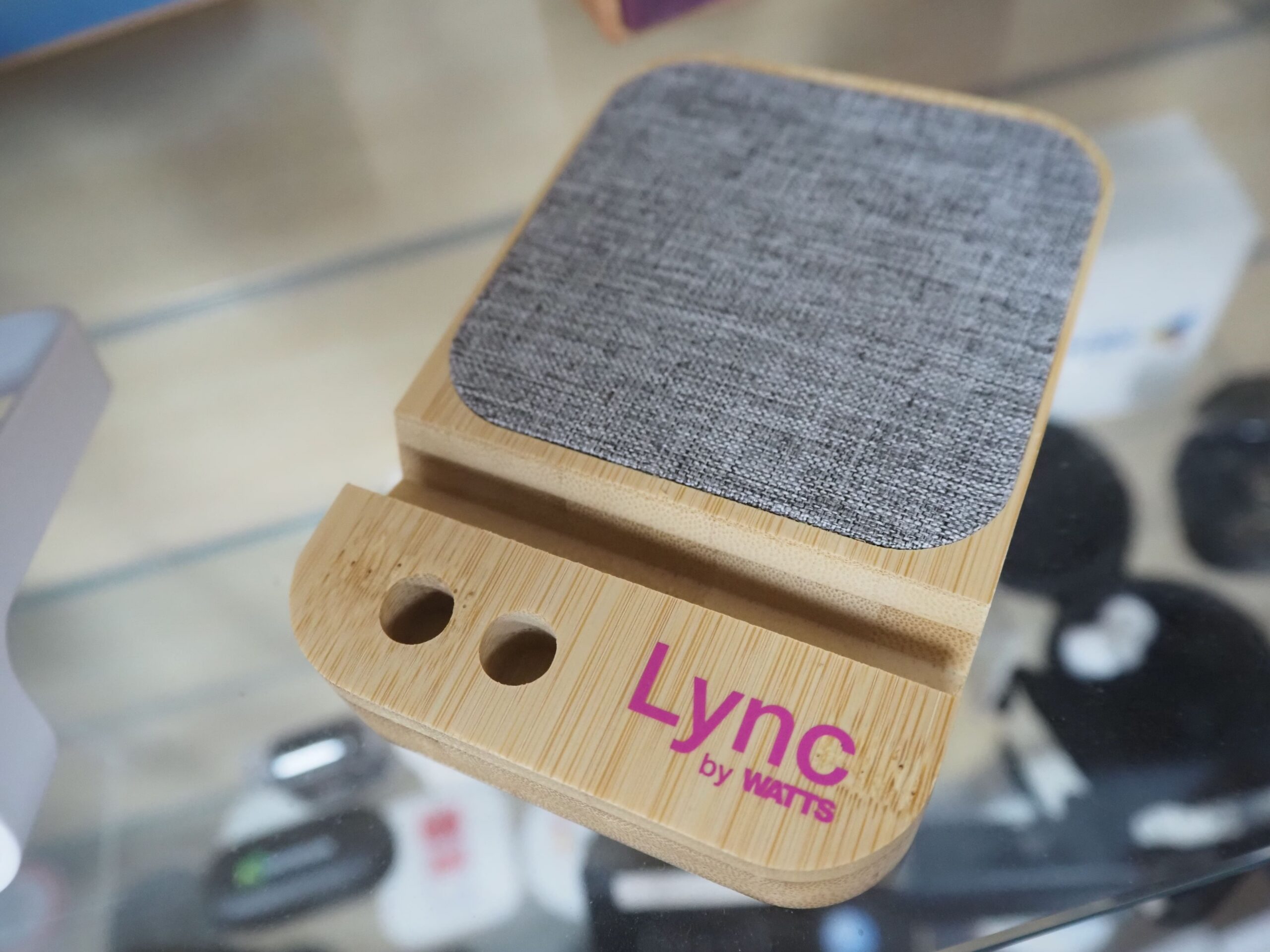 A wooden phone stand with fabric top, labeled Lync by watts in pink—perfect Physical Merchandise.