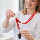 Smiling woman holds keys on a red Premium Woven Lanyards with key fob attached.