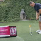 Man putting on green lawn; Golf Balls Srixon Tri box visible in foreground.