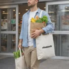 Man carries grocery bags, including a Recycled Cotton Tote Bag, outside a store.