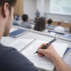 Student taking notes with a Waterman Hemisphere Series pen in a lecture hall.