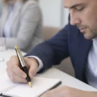 Man in a suit writes with a Parker Pens Frontier Stainless Steel Gold Trim at a meeting.
