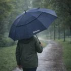 Person walks in the rain, holding a navy Fonza 62Inch Vented Golf Umbrella.