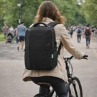 Person with a black Swissdigital Arosa Backpack rides a bike on a tree-lined park path.