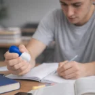 Young man writes in a notebook, squeezing the Stress Pill Capsule for stress relief at his desk.
