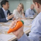 Person holds Stress Balls - Carrot during a meeting at a conference table with colleagues.