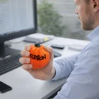 Person holding a Pumpkin Stressballs toy at a computer desk.
