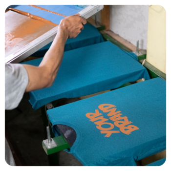 A person screen-printing YOUR BRAND on durable golf shirts in blue with orange ink.