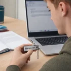 Person holding a Slim Swivel Usb Flash Drive near an open laptop and notebook.