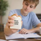 Teen studying at a desk holding a Stress Balls Bread Slice with YOUR LOGO HERE text.