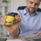 Man holding Sports Car Yellow toy near a laptop at a desk, with Your Logo Here on it.