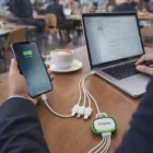 A person charges a phone and laptop in a café using Chipley 4-In-1 Charging Cables.