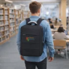 Person with a black Compact Logo Emblazoned Daily Bag stands in a library with bookshelves.