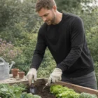 Man gardening in Men's Murano L/S Tees, wearing gloves and planting in a raised garden bed.