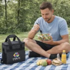 Man enjoying salad on picnic blanket with Ventura Coolers, fruit, sandwich, and juice.
