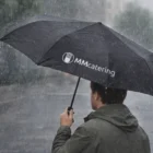 Person holding a Gleek Auto Open/Close Umbrella in the rain on a city street.