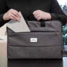 Person placing a notebook into a gray laptop bag labeled House of Revolutions.