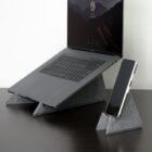 A laptop and a smartphone on separate gray fabric stands on a dark desk.