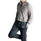 Man wearing a gray shirt and dark pants with a phone hanging on a neck strap.