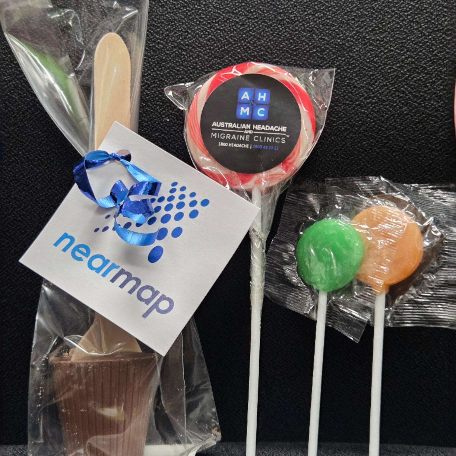 Assorted lollipops and a chocolate treat—top promotional items 2025 with Nearmap tag and ribbon.