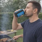 Man grilling outdoors, drinking with Magnetic Coolers nearby and a customizable logo cup holder.