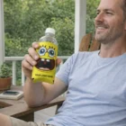 Smiling man holds water bottle in a Life Jacket Coolers sleeve on a porch.