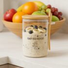 Glass jar of overnight oats with banana and blueberries, with fruit bowl in the background.