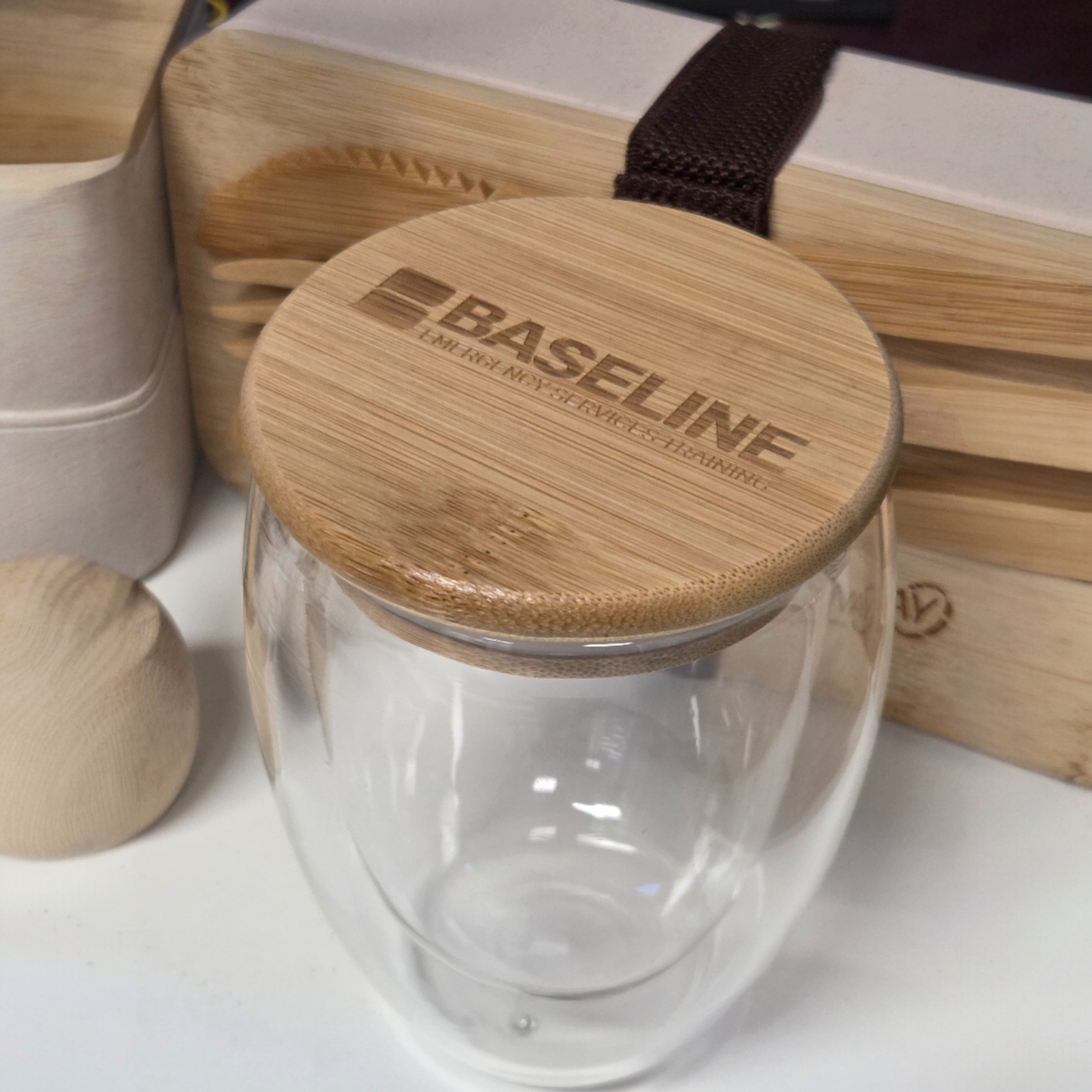 A glass cup with a bamboo lid labeled "Baseline" shows print vs. engraving next to utensils.