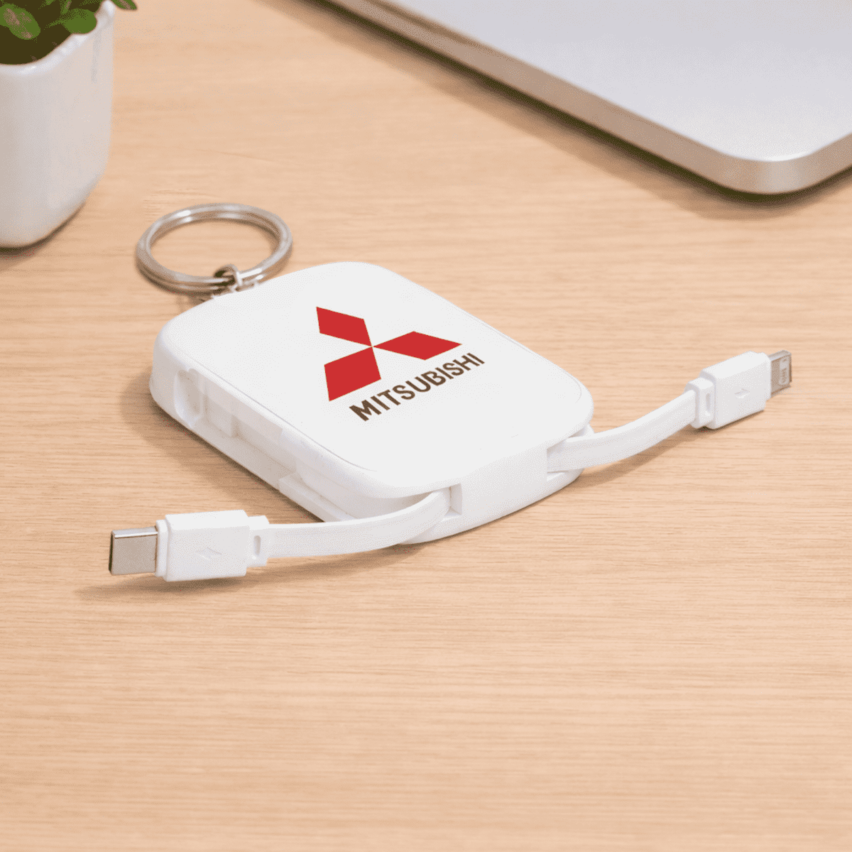 lifestyle-43.png White Mitsubishi-branded keychain with attached USB-C and Lightning charging cables on a desk.