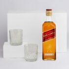 A bottle of Johnnie Walker Red Label with two empty whisky glasses on white blocks.