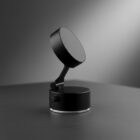 A modern, black, circular desktop microphone on a round base, with a minimalistic design.