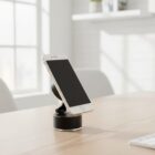 Smartphone on a black stand placed on a wooden desk in a bright, sunlit room.