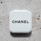 A white Chanel compact case on a light stone surface.