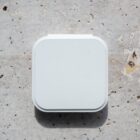 A white, square object on a light, textured stone surface, casting a shadow below.
