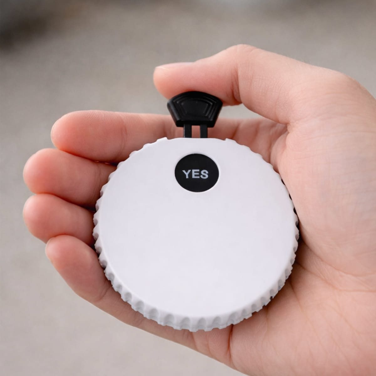 A hand holding a round white device with a black button labeled YES on top.