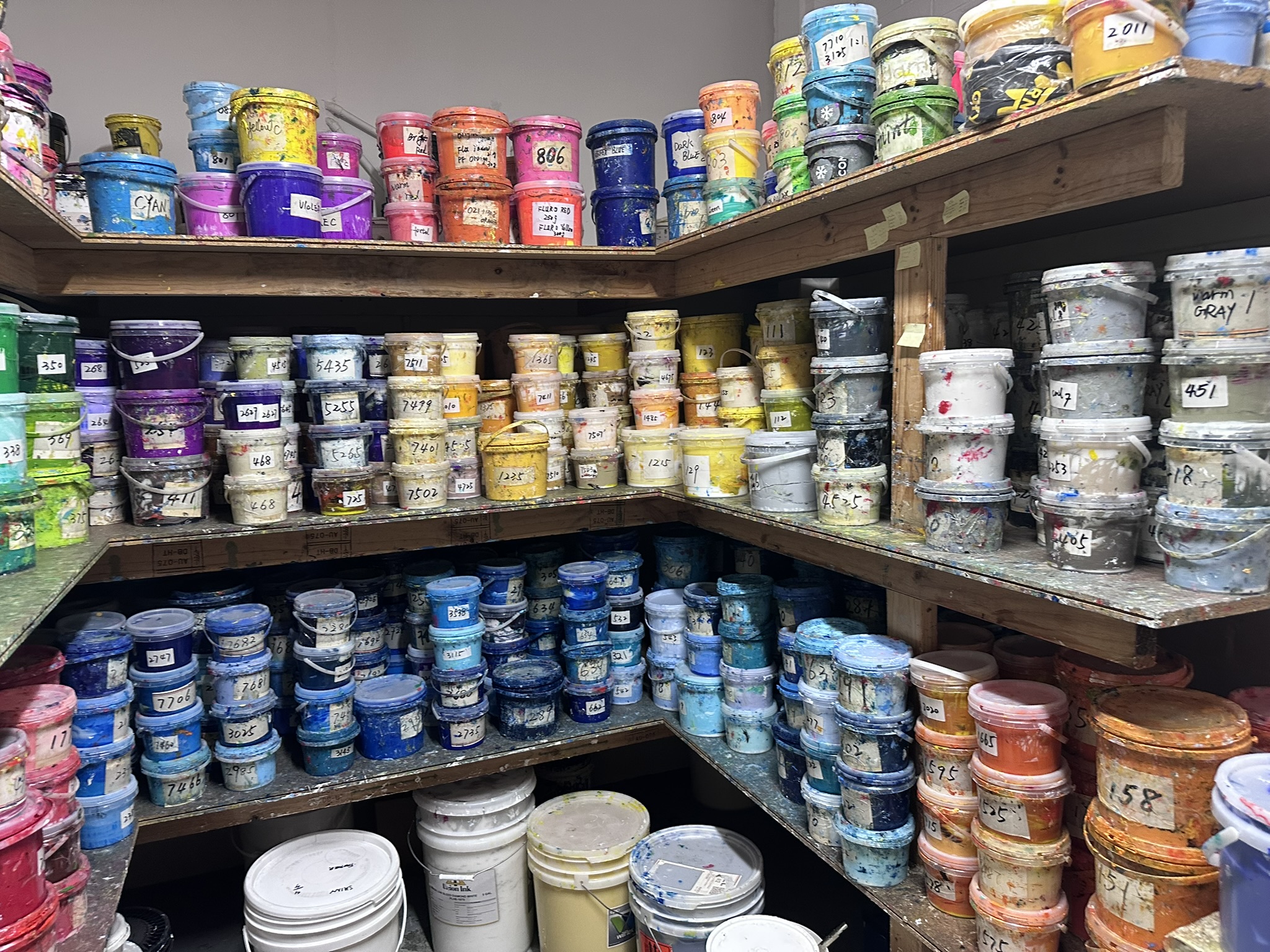Shelves filled with colorful paint containers, organized by shade for print vs. engraving projects.