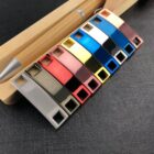 Ten colorful USB flash drives in a row on a black surface beside a pen and wooden item.