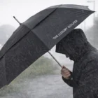 Person holding The Luxury Golfer black umbrella, showcasing a luxury golf lifestyle.