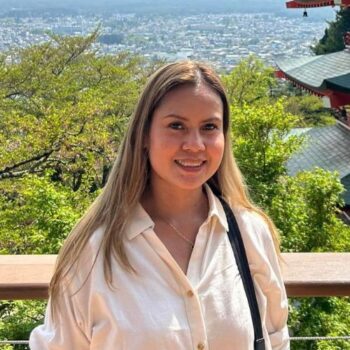 Meet the team: Woman in a white shirt smiling outdoors with trees and city views behind her.