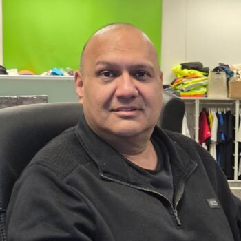 Meet the team: A man sits in an office chair, with clothes and a green wall behind him.