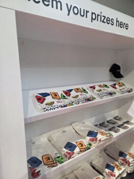Shelves displaying folded white t-shirts with colorful graphics and a black cap on the top shelf.